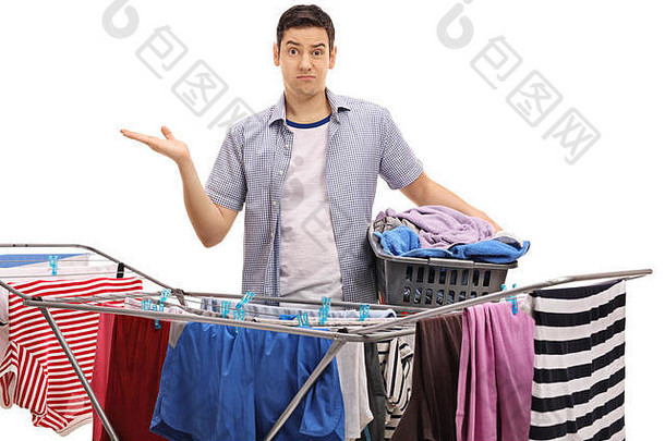 一个困惑的家伙拿着一个洗衣篮，用手在一个白色背景的晾衣架后面做手势