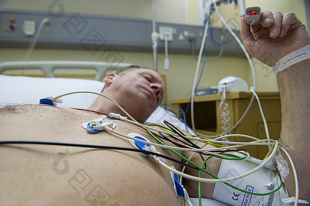 一名男子躺在医院的病床上，用心脏监护仪评估心脏病发作的风险，他的脉搏在手指上测量