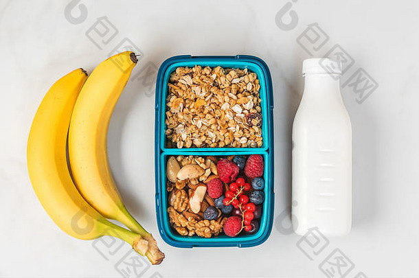 健康的午餐盒，有格兰诺拉麦片、坚果、浆果、香蕉和酸奶，在白色背景上做健康的早餐。俯视图