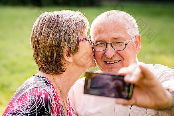 幸福的老年夫妇用智能手机拍照——女人在亲吻男人