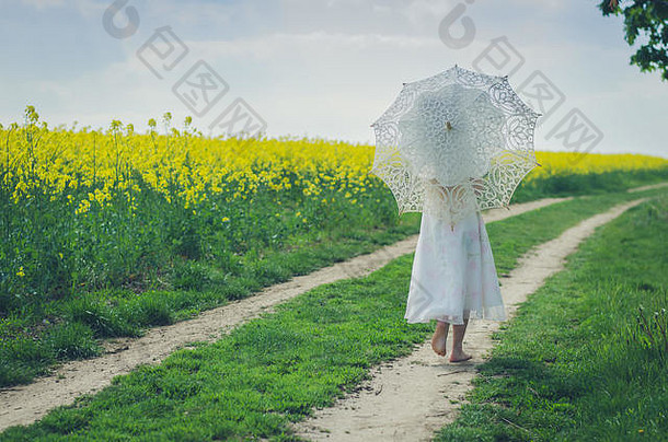 在乡村小路上的孩子用白色蕾丝雨伞保护自己免受阳光的伤害