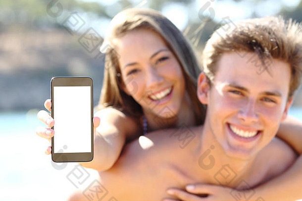 海滩上的幸福夫妇在暑假展示空白手机屏幕