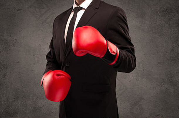 一位穿着考究的销售人员手戴红色拳击手套站在城市灰墙背景前。