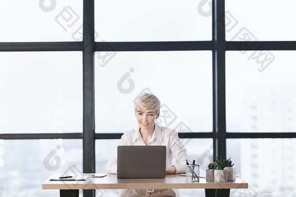 快乐的女商人在现代办公室里用笔记本电脑工作