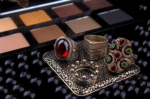 化妆工具和银配件在毛皮黑色背景/特色眼影调色板，银戒指和耳环在一个愤怒的黑色背景