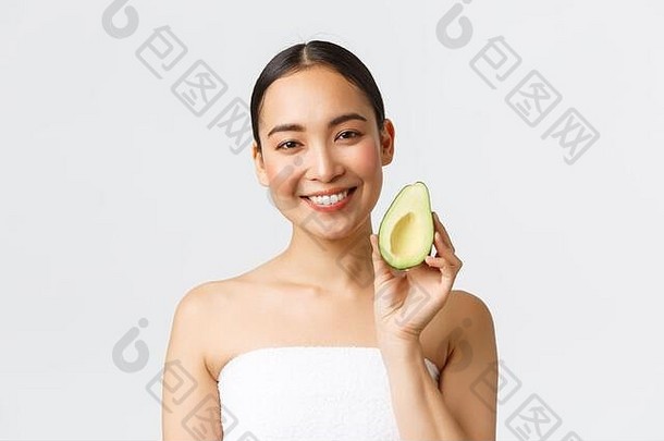 美容、个人护理、水疗和护肤概念。漂亮的亚洲女孩站在浴巾上，表情清新，展示鳄梨和微笑的特写镜头