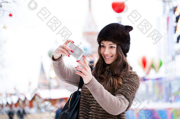 俄罗斯，莫斯科克里姆林宫，背景红场上，年轻美丽的女游客用手机拍照
