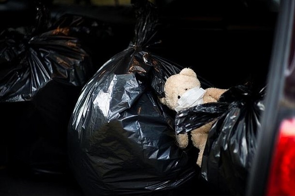 一只戴着医用面具的泰迪熊躺在汽车行李箱的垃圾袋上