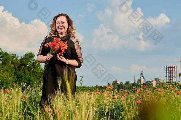 在绿色小麦和野地上，一位长发、身材匀称的黑衣女人。超重的胖女人。自由和新鲜的概念。