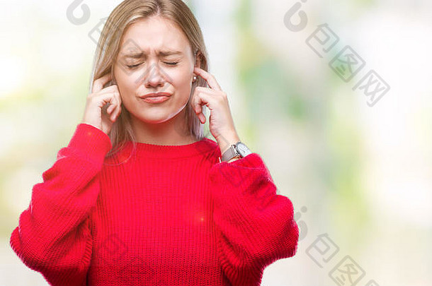 一位年轻的金发女郎，穿着冬衣，隔着孤立的背景，用手指捂住耳朵，对嘈杂的音乐声表现出恼怒的表情。缉毒局