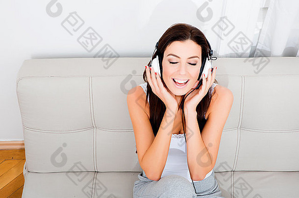 年轻漂亮的女人坐在沙发上，戴着耳机听音乐
