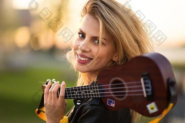 美丽的女人在日落时带着吉他