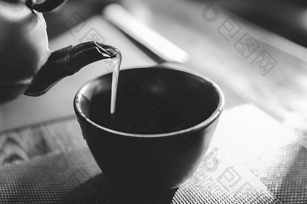 特写镜头：在桌上的一个东方风格的杯子上倒一个热的日本绿茶壶-自然光