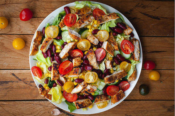 鸡肉沙拉的特写镜头和盘子里的新鲜蔬菜，木质背景，俯视图