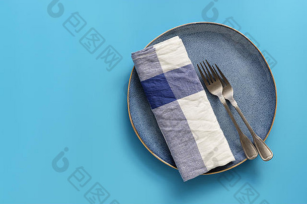 蓝色的空盘子，格子餐巾和叉子在柔和的蓝色背景上。俯视图、平面布局、空间