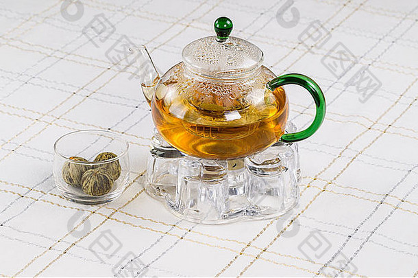 背景为白色条纹桌布的玻璃茶壶、茶座和茶球的水平照片