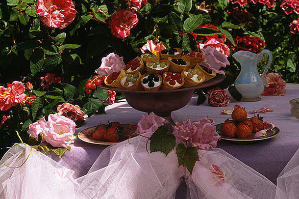 花园餐桌上底座上的小蛋糕的静物画，白色欧根纱包裹，粉色玫瑰装饰