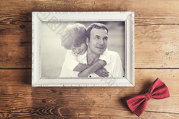带家庭照片的相框和放置在木制背景上的虚线领结。