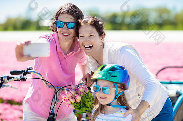 荷兰一家人在荷兰郁金香花圃里骑自行车。母亲和孩子们在花开的自行车上用手机拍照自拍