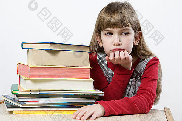 有可能读所有这些书吗？桌旁坐着一堆书的可爱悲伤的小女孩。