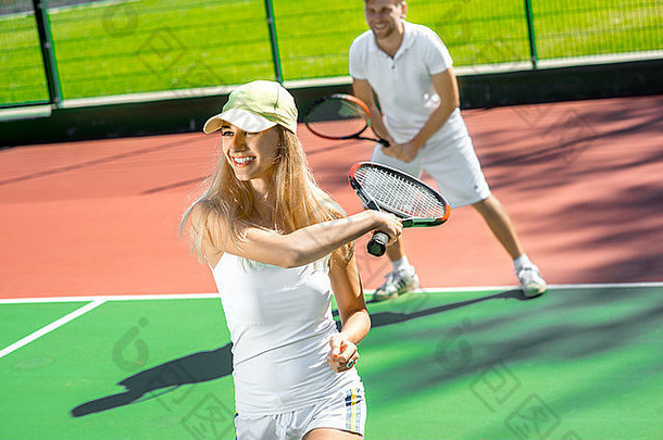 夏天，一对穿着白色运动服的年轻夫妇在外面的网球场上打网球