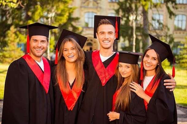 五位身着长袍、戴着帽子、微笑着拥抱的成功毕业生