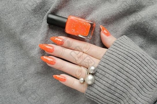 有着长长指甲和橙色姜黄色指甲的女人手上拿着一瓶指甲油