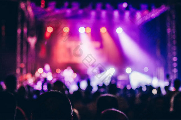 音乐会人群参加音乐会时，人们的轮廓清晰可见，舞台灯光为背景照明。举手和智能手机随处可见。