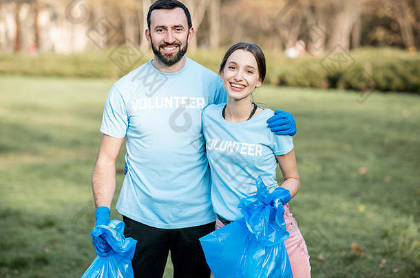 公园清洁后，穿着蓝色t恤衫的快乐志愿者与装满垃圾的袋子站在一起的照片