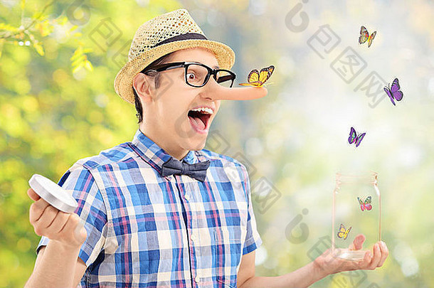 兴奋的男人把蝴蝶从户外的罐子里放出来，把注意力集中在站在他鼻子上的那个蝴蝶上