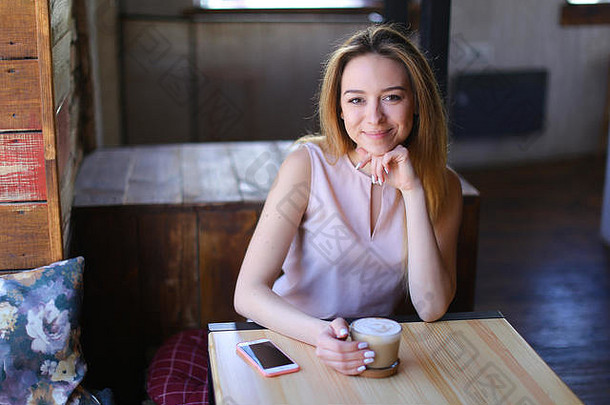 美丽的女坐着木表格白色智能手机杯咖啡舒适的咖啡馆