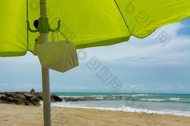 面罩放在海滩和蓝天的岸边的伞下，背景是一些云。pa期间的新标准概念