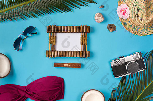 相框，帽子，照相机，太阳镜，椰子，蓝色背景。蓝色背景上的海滩主题。顶视图。