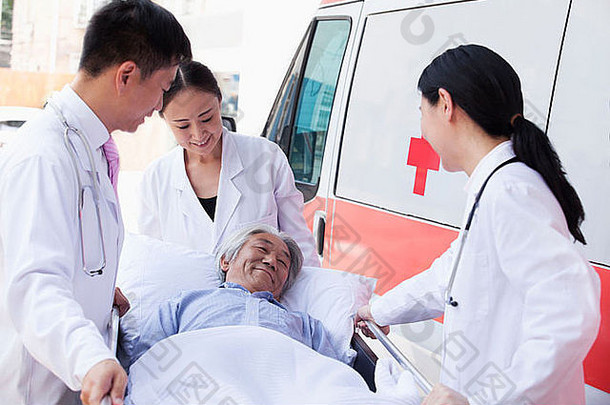 三<strong>名医</strong>生在救护车前用担架抬着一名老年病人