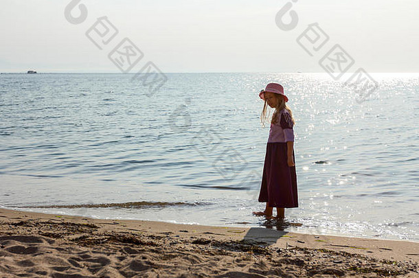 年轻的女人，戴着帽子的孩子，穿着可爱的夏装，光着脚站在浅水区的海边。