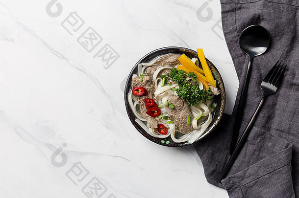 亚洲汤，碗里有面条、肉和蔬菜，白色背景上有餐巾和餐具。水平俯视图，文本可用空间