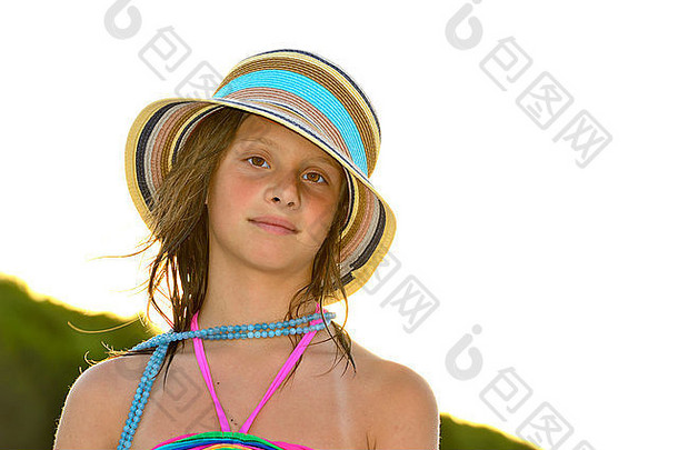 日落时海滩上的小女孩，戴着大帽子微笑着。