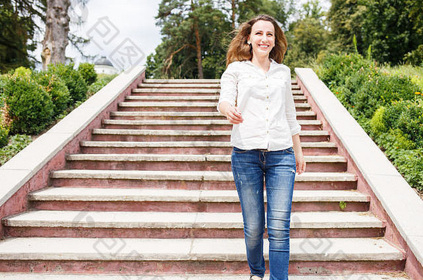 穿着白衬衫的快乐年轻女子从公园的楼梯上下来