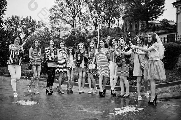 十一位漂亮的辫子女郎和可爱的新娘在公园里用香槟庆祝单身派对。黑白照片。