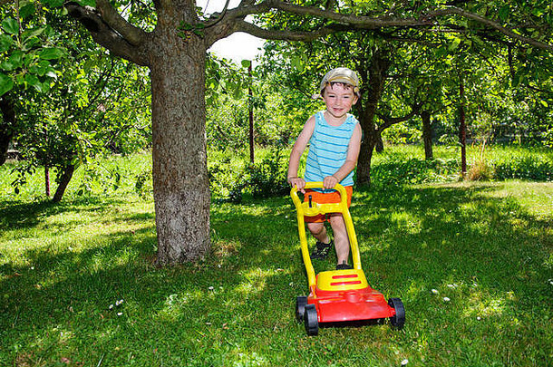 阳光明媚的日子里，快乐的小男孩用他的割草机帮助园艺，脱下t恤，头上戴着小结的手帕