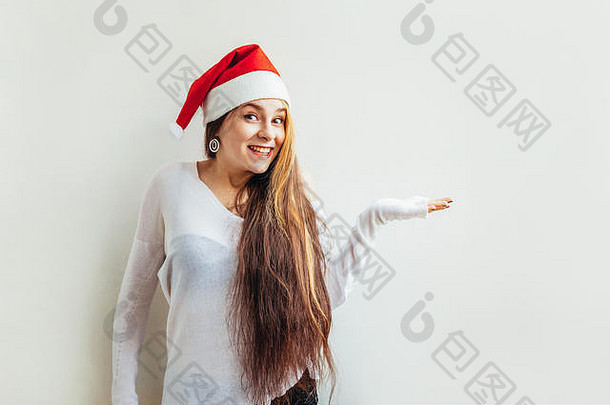 美丽的女孩，长发，戴着红色圣诞老人帽，手掌张开，白色背景。年轻女子肖像，真实情感。圣诞快乐，新年快乐。