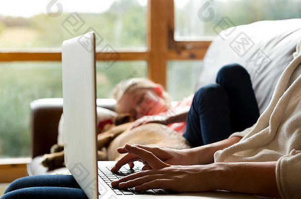 一名妇女使用笔记本电脑，她的女儿和宠物<strong>狗</strong>睡在她旁边