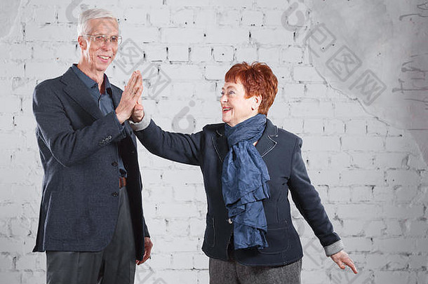 击掌。一对幸福微笑的老夫妇站在白色的砖块背景上，依偎在一起。空间。
