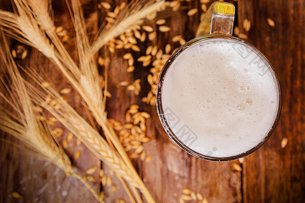 上图：一杯泡沫淡啤酒，背景是一根麦枝和一张木桌上的小麦