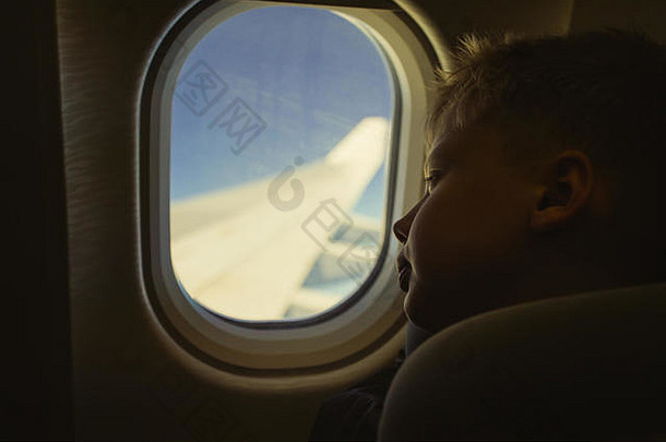 飞行中，坐在座位上看着窗户的可爱的金发白孩子。彩色摄影以复古风格过滤。