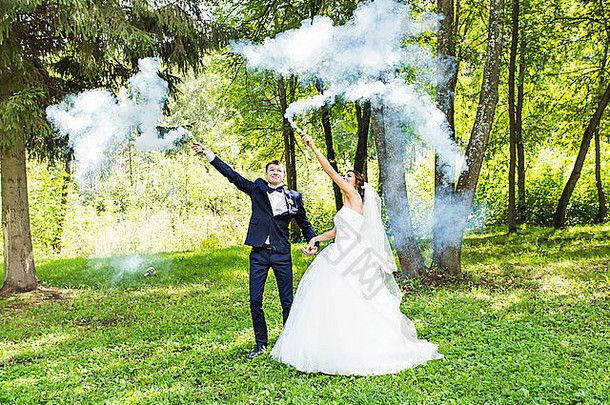 婚礼，爱情，人际关系，婚姻。带着蓝色烟雾微笑的新娘和新郎