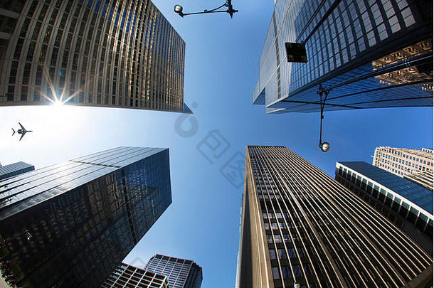 从城市街道到晴朗天空的低角度视图，高大摩天大楼的玻璃和<strong>钢立面</strong>，以及天空中的平面
