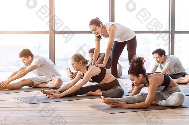 瑜伽教练在小组课上帮助年轻女子做伸展运动