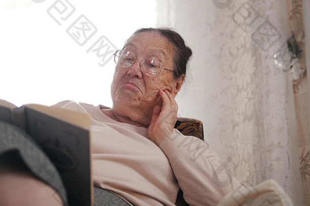 一位戴眼镜的老妇人坐在扶手椅上看书