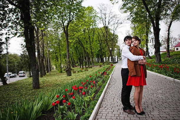 夫妇拥抱爱路径郁金香花花园时尚的男人。天鹅绒夹克女孩红色的衣服爱